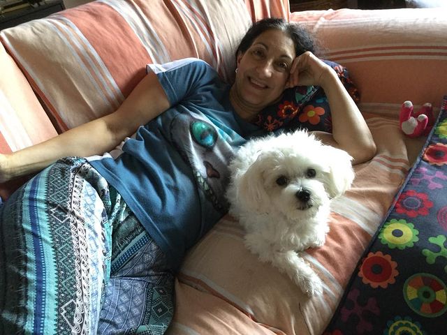 Elena Seijo in a blue t-shirt and pants lying on a sofa with her pet looking at the lens.